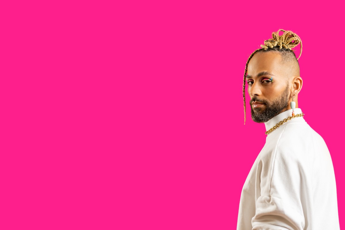 A practitioner in a flat cap and casual shirt against a hot pink background