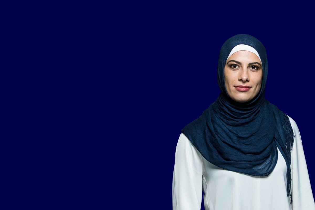 A practitioner in a pale blue head covering and denim with a calm, contemplative presence against a marine background