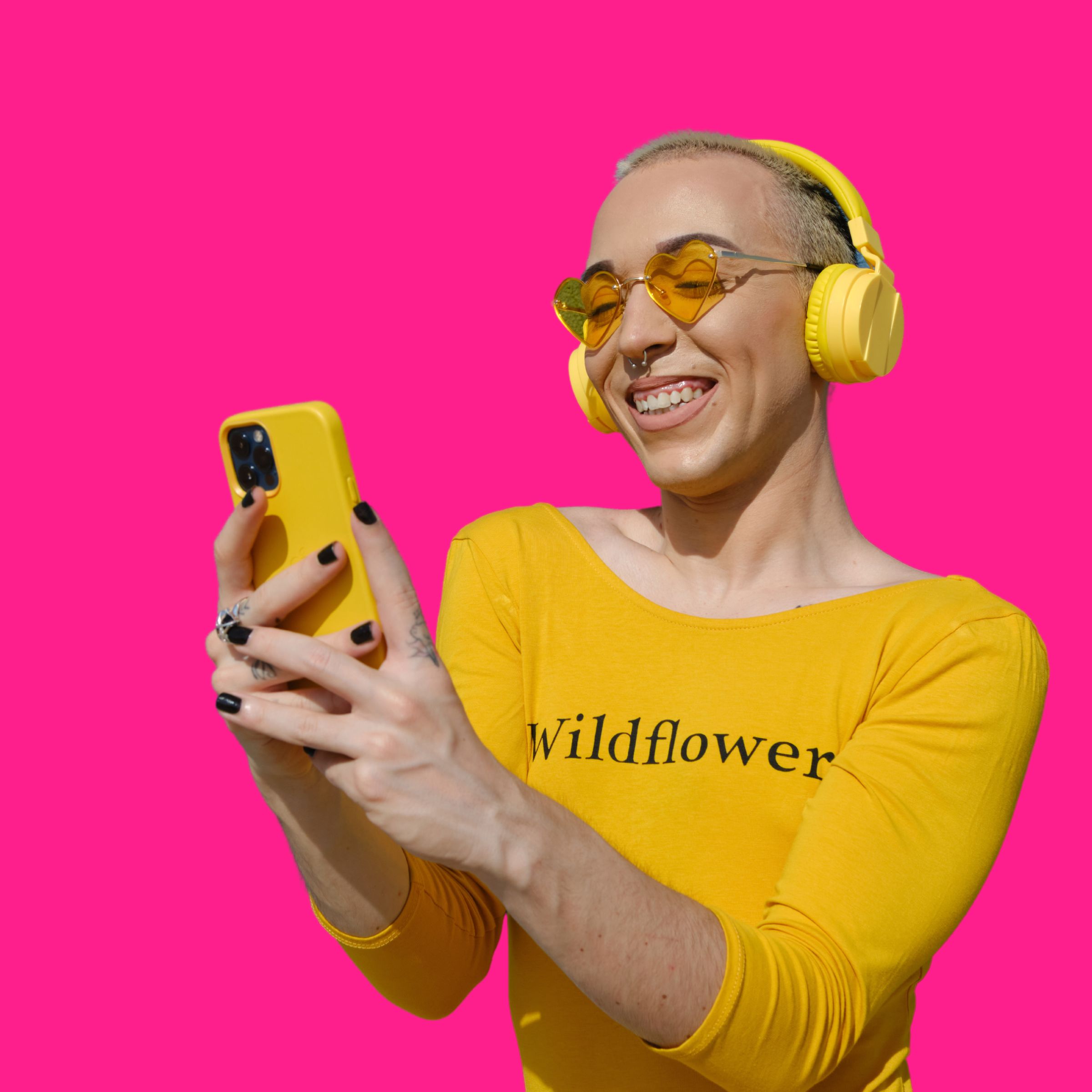 A smiling person in a yellow shirt taking a selfie against a hot pink background