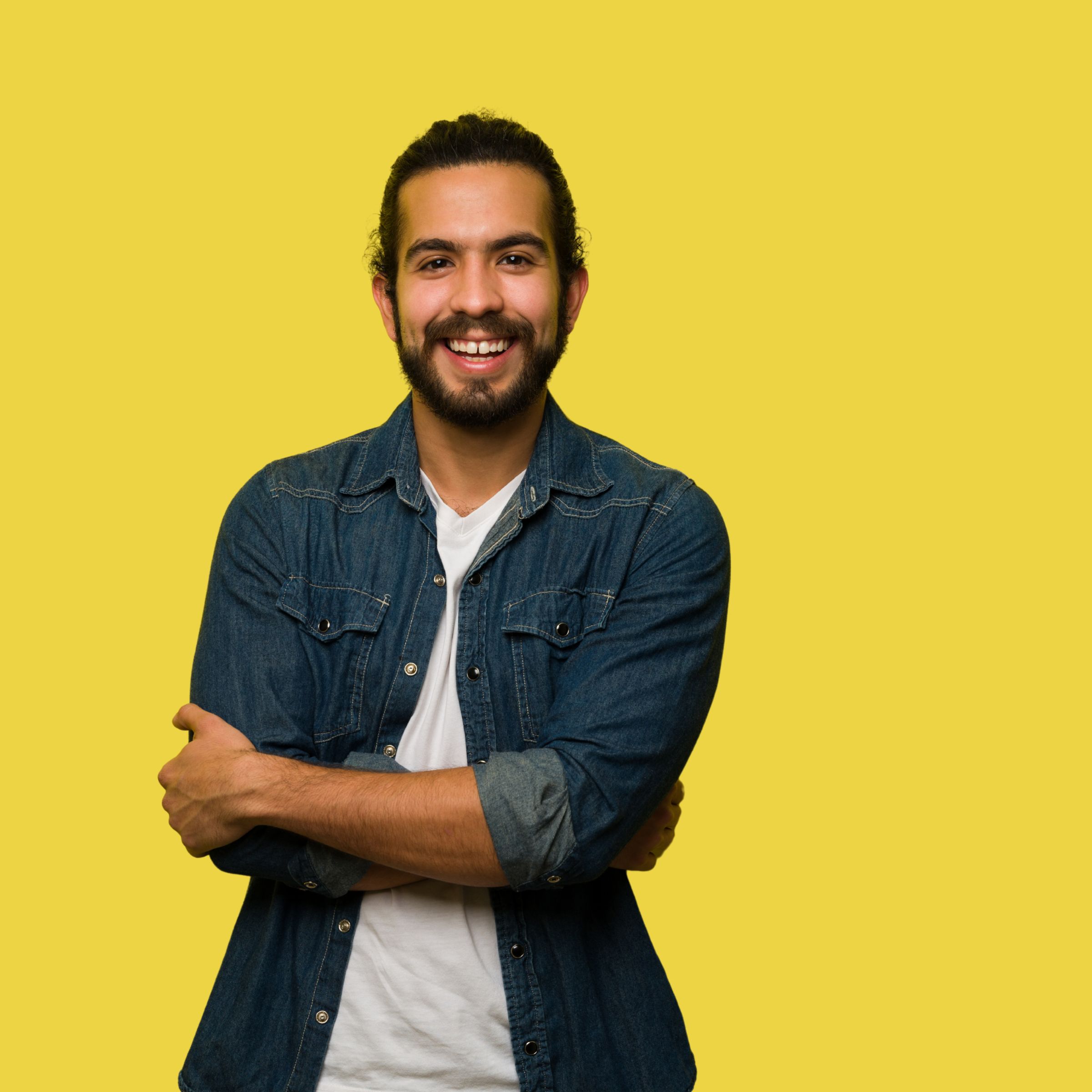 A bearded man in a denim shirt smiling with arms crossed against a yellow background