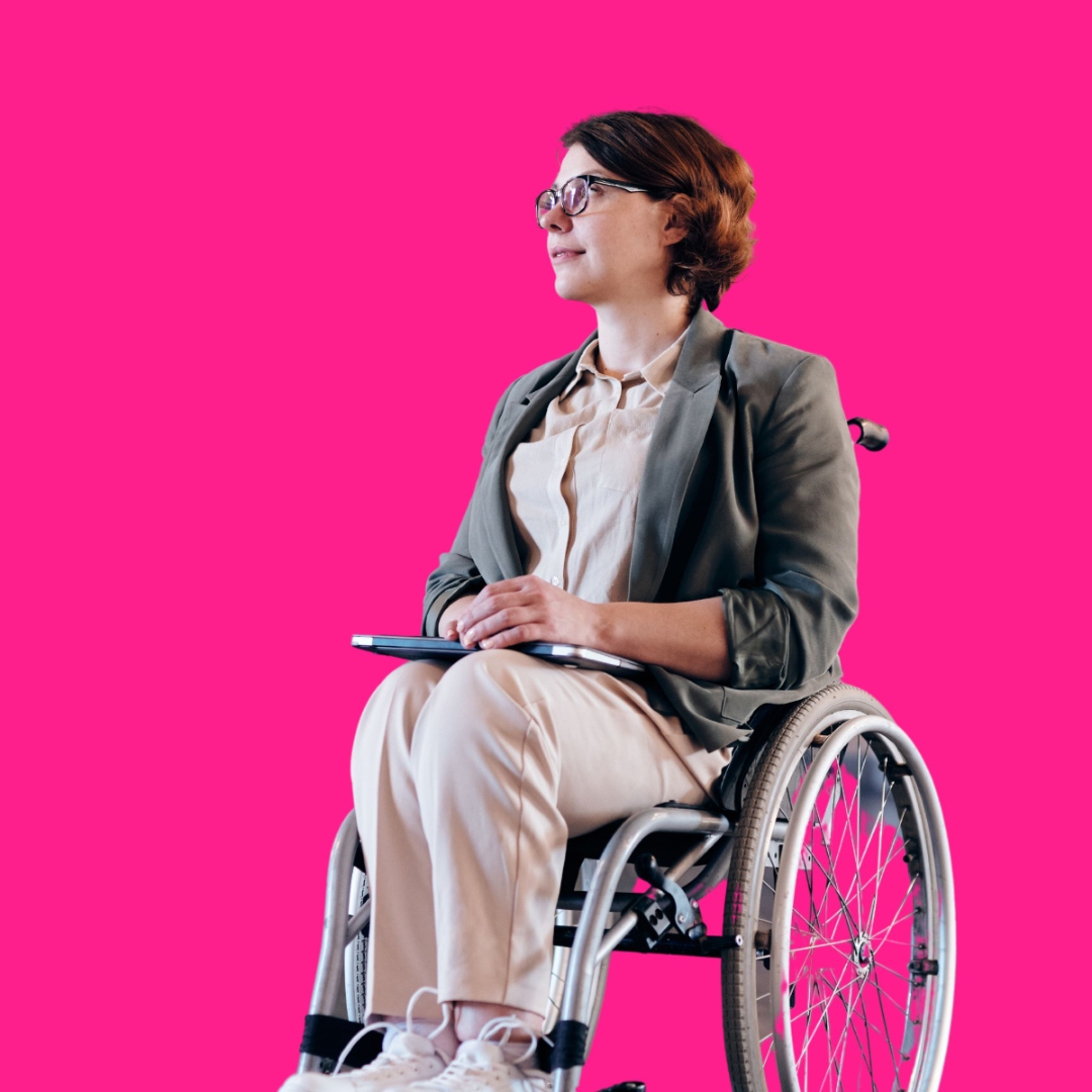 A professional woman in glasses and a blazer using a wheelchair, holding a tablet on her lap and looking off camera, against a hot pink background